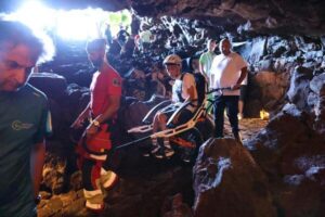 Deportistas con discapacidad disfrutan de una visita adaptada a la Cueva de los Verdes en Lanzarote 2 Persona en una silla Joëlette acompañada por varias personas de apoyo durante la visita adaptada a la Cueva de los Verdes, en un tramo de terreno rocoso.
